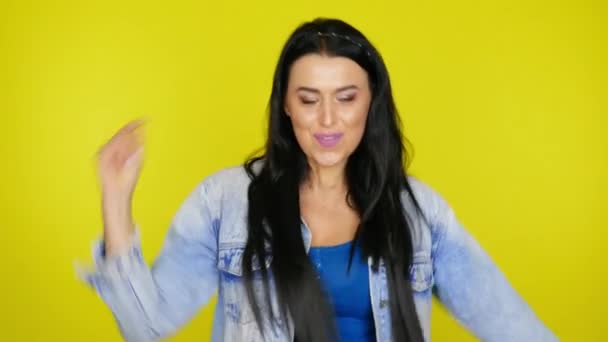 Frau mit schwarzen Haaren in Jeansjacke tanzt auf gelbem Hintergrund — Stockvideo
