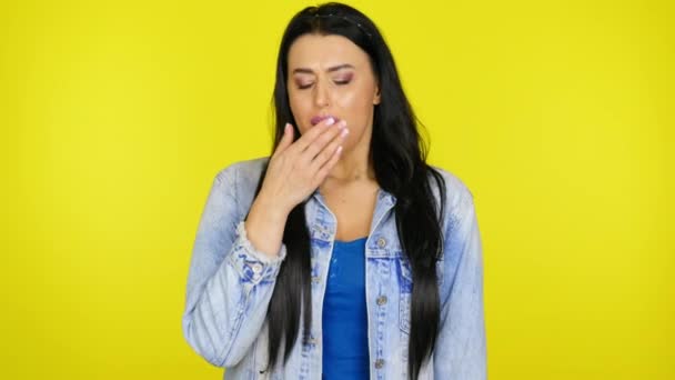 Mujer bosteza cubriéndose la boca con palma sobre un fondo amarillo con espacio para copiar — Vídeo de stock