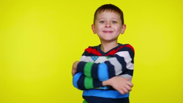Веселый маленький мальчик обнимает коробку с подарком и улыбается на желтом фоне — стоковое видео