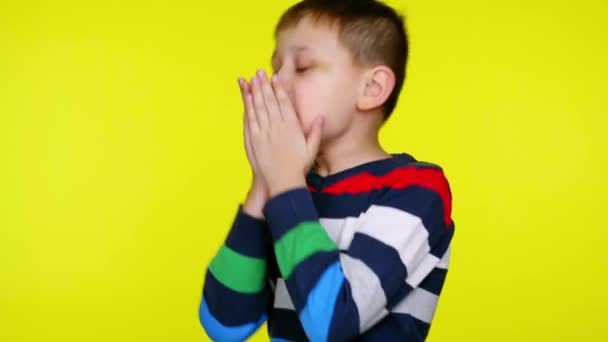 Niño enfermo estornuda y se cubre la boca con palmas sobre un fondo amarillo — Vídeos de Stock