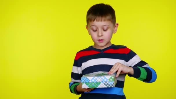 Niño pequeño abre caja con un regalo y se sorprende sobre un fondo amarillo — Vídeos de Stock