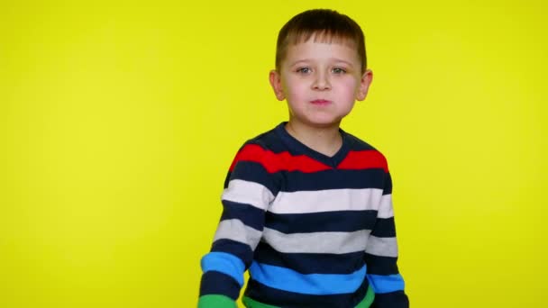 Bambino ragazzo mangia cioccolato e lancia un involucro alla fotocamera su sfondo giallo — Video Stock