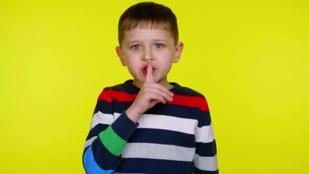 Zwijg. klein kind jongen zet index vinger naar zijn lippen op een gele achtergrond — Stockvideo