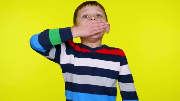 小さな子供の男の子は驚いています彼の口を閉じて手のひらで黄色の背景 — ストック動画