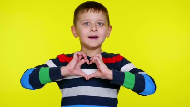 Child boy folds heart near chest with fingers and smiles on yellow background — Stock Video