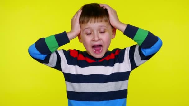 Mały chłopiec krzyczy trzymając głowę w dłoniach na żółtym tle. — Wideo stockowe