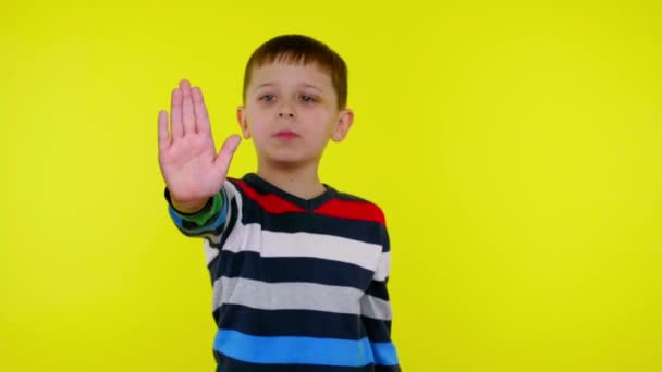 Ragazzo bambino serio alza la mano con il palmo e dice STOP su uno sfondo giallo — Video Stock