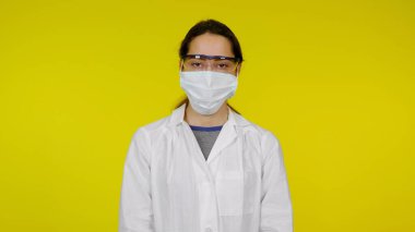 Koruyucu tıbbi maskeli, gözlüklü ve beyaz önlüklü genç bir doktor.