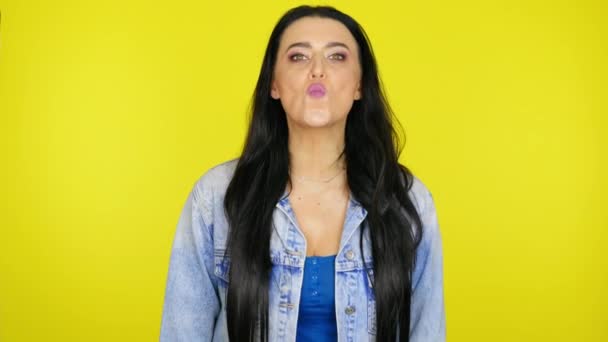 Femme aux cheveux noirs dans une veste en denim embrasse sur un fond jaune — Video