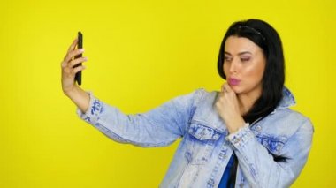 Kadın poz veriyor ve akıllı telefondan selfie çekiyor. Sarı arka planda, kopyalama alanı olan.