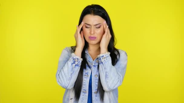 Kopfschmerzen. Frau massiert ihre Schläfe mit den Fingern auf gelbem Hintergrund — Stockvideo