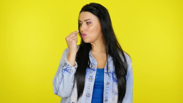 Woman puts gum in mouth and starts to chew with pleasure on a yellow background — Stock Video