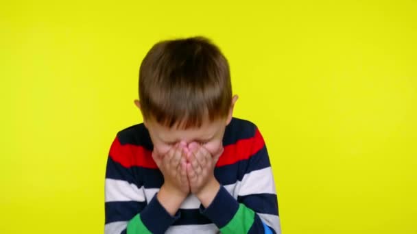 Niño enfermo estornuda y se cubre la boca con palmas sobre un fondo amarillo — Vídeos de Stock