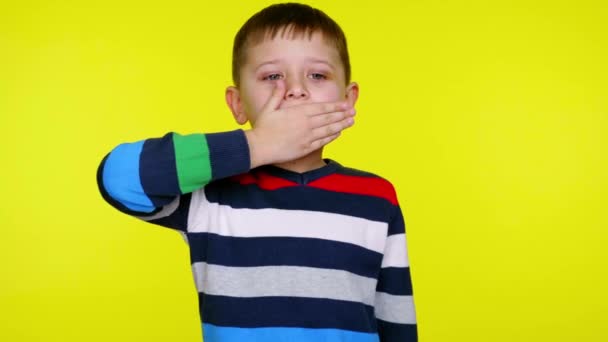 Little child boy covered his mouth with his palm and stands on yellow background — Stock Video