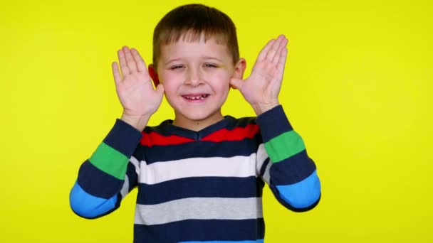 Lustig liten pojke tar bort händerna från ansiktet och ler på gul bakgrund — Stockvideo
