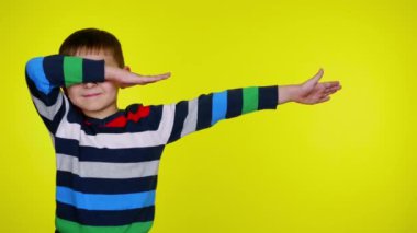 Neşeli çocuk dans ediyor DAB yapıyor ve sarı arka planda gülümsüyor.