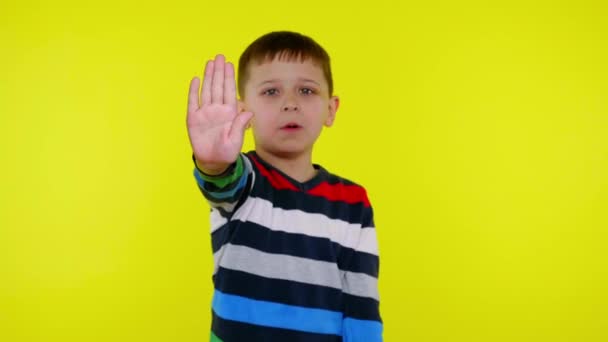 Niño serio levanta la mano con la palma y dice DETENER sobre un fondo amarillo — Vídeos de Stock