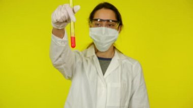 Beyaz elbiseli kadın, koruyucu maske test tüpünün içindekileri inceliyor.
