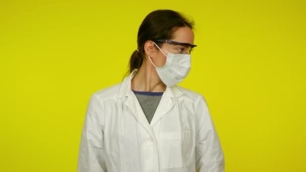 Jeune femme en manteau médical, masque de protection danse sur fond jaune — Video