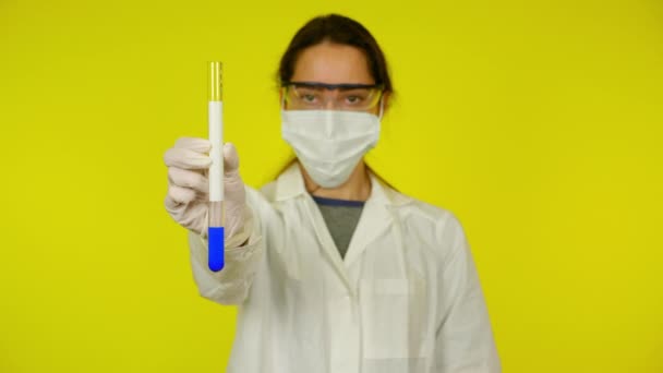 Woman in medical gown, protective mask is shows test tube with space for text — Stock Video