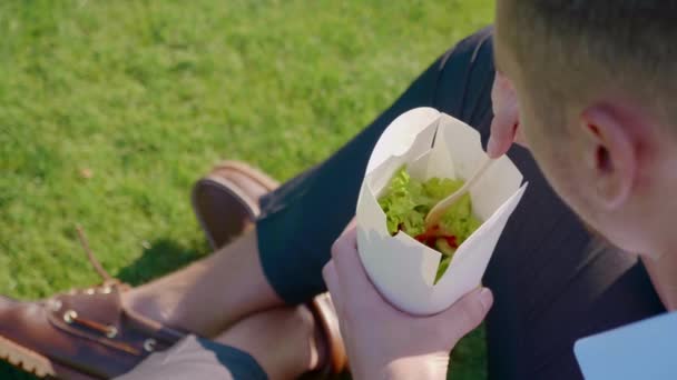 Businessman eats vegetables with paper ecological packaging with a wooden fork — Stock Video