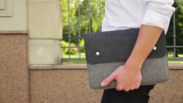 Un hombre de negocios cercano con un portátil en la mano camina por el parque — Vídeo de stock