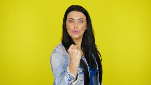Vrouw toont een vuist op de camera op een gele achtergrond met kopieerruimte — Stockvideo
