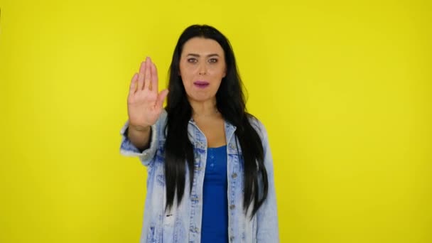 Serious woman raises hand with palm and says stop on yellow background — Stock Video