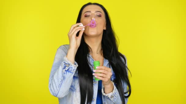 Woman inflates soap bubbles and smiles on a yellow background with copy space — Stock Video