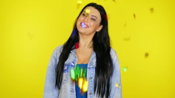 Kvinna poserar och tittar på konfetti faller framför henne på en gul bakgrund — Stockvideo