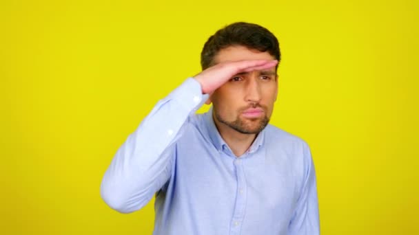 Knappe man met baard kijkt om zich heen met zijn hand op het voorhoofd op gele achtergrond — Stockvideo