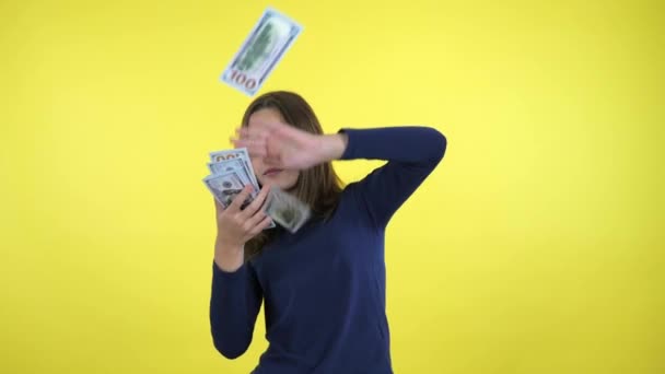 Rich teenager girl in a blue sweater scatters lot of money on yellow background — ストック動画