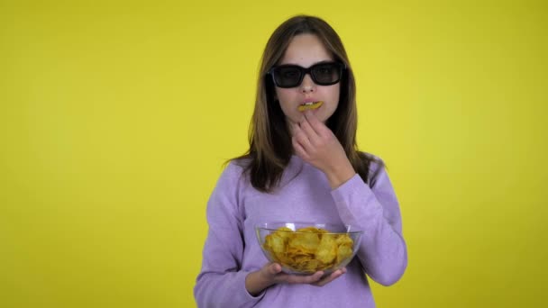 Meisje lacht kijkt film in zwart 3D bril, eet aardappel chips uit glazen schaal — Stockvideo