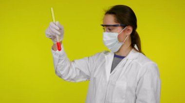 Koruyucu maskeli kadın test tüpünün içeriğini inceliyor ve kafasını çeviriyor.