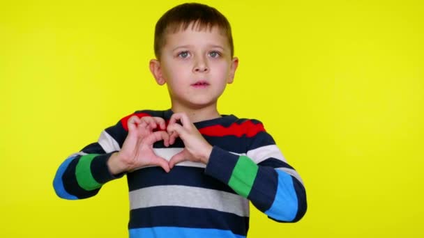 Niño niño pliega el corazón cerca del pecho con los dedos y sonrisas sobre fondo amarillo — Vídeo de stock