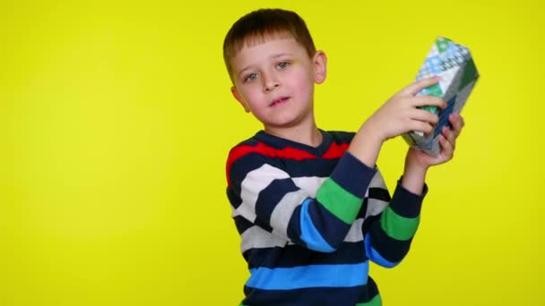 Kind jongen lafaards doos met een geschenk in de buurt van oor proberen te begrijpen wat er in zit — Stockvideo