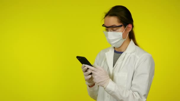Женщина в медицинском пальто, защитная маска удивила то, что она увидела на смартфоне — стоковое видео
