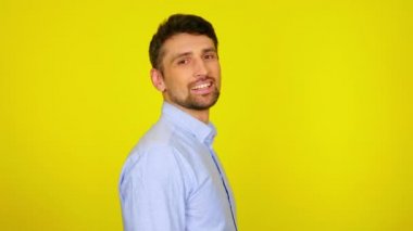 Yakışıklı sakallı adam başını kameraya çevirir ve sarı arka planda gülümser.