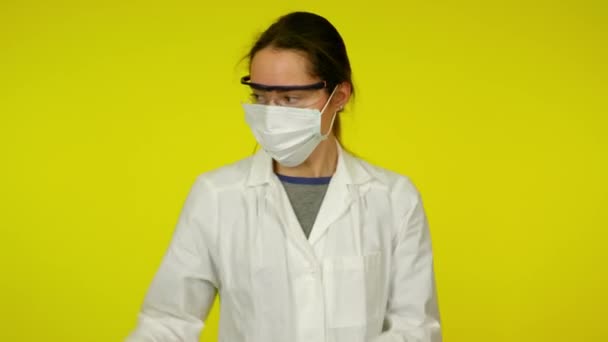 Jovem mulher de casaco médico, máscara protetora está dançando em fundo amarelo — Vídeo de Stock