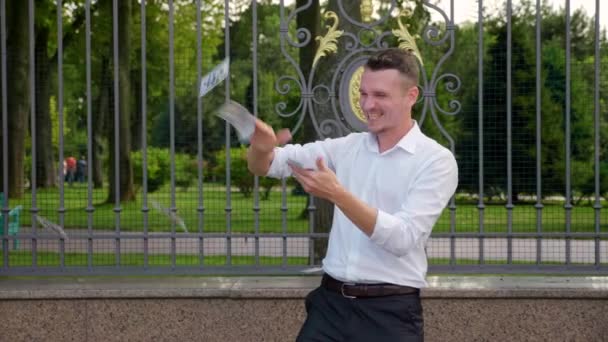 Jonge zakenman strooit dollars in een park. 4K-beelden — Stockvideo