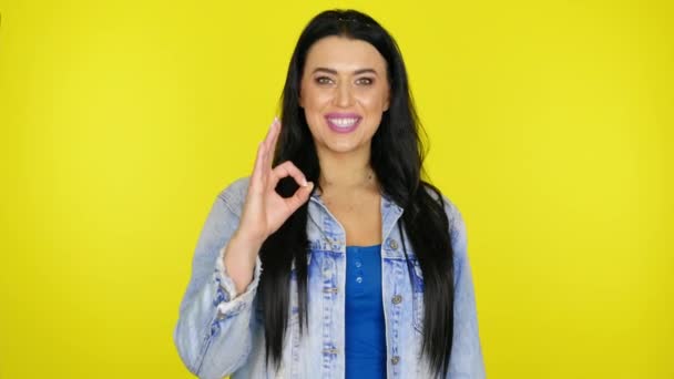 Kvinna ler och visar okej på en gul bakgrund med kopia utrymme — Stockvideo