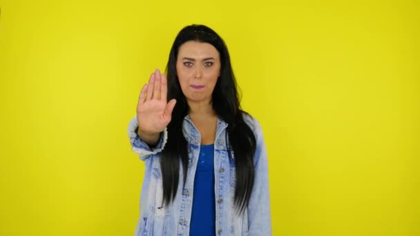 Seriös kvinna höjer handen med handflatan och säger stopp på gul bakgrund — Stockvideo