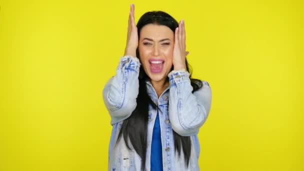 Žena křičí, opírá ruce o hlavu na žlutém pozadí s kopírovacím prostorem — Stock video