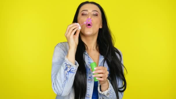 Mujer infla burbujas de jabón y sonríe sobre un fondo amarillo con espacio de copia — Vídeos de Stock