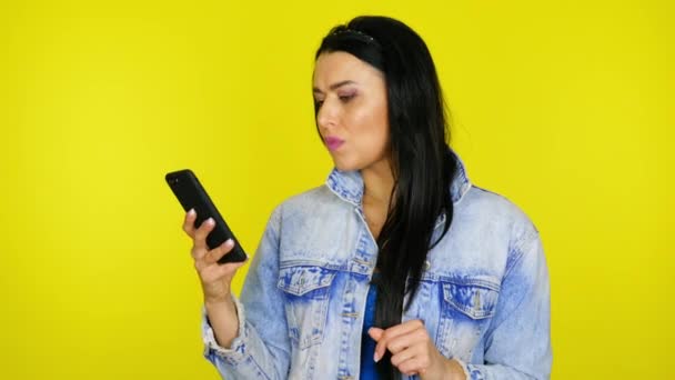 Mujer utiliza un teléfono inteligente y luego se sorprende y dice wow sobre un fondo amarillo — Vídeos de Stock
