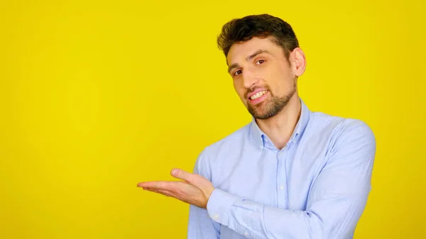 Homem de camisa azul claro sorri e mostra com a mão um lugar para produtos e texto — Fotografia de Stock