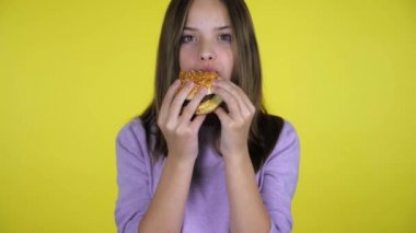 Pembe kazaklı genç kız sarı arka planda fotokopi alanı olan bir burger yiyor.