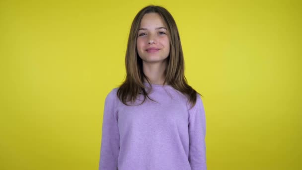 Tiener meisje in een roze trui glimlacht en kijkt naar de camera op gele achtergrond — Stockvideo