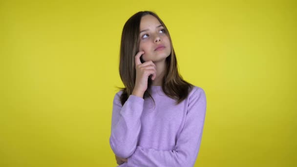 Menina levanta a mão, descansa o dedo na bochecha, olha em volta e pensa o que escolher — Vídeo de Stock