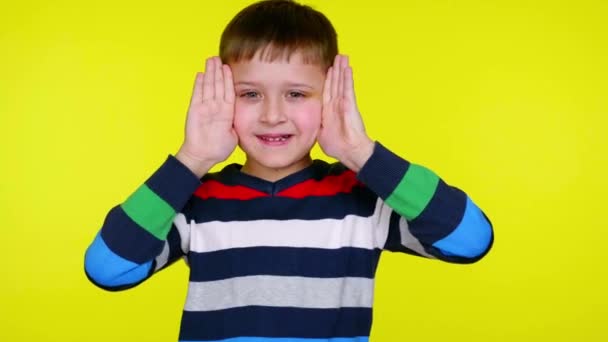 Funny little child boy takes hands off his face and smiles on yellow background — Stock Video